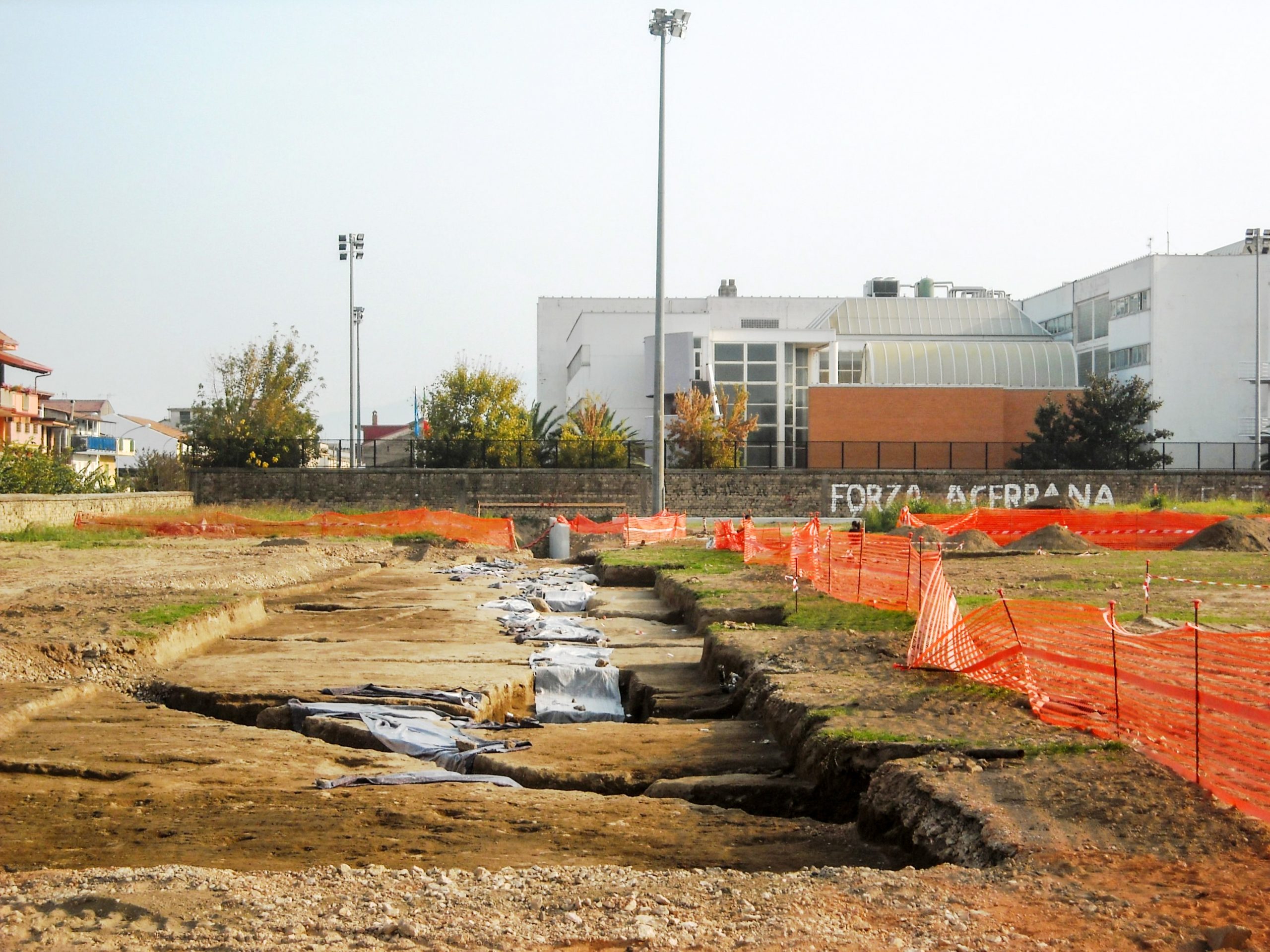 l'antica città romana di Acerra emersa dal campo sportivo, allo spalle il palazzo del Comune